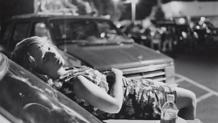 black and white photo of young woman laying on the hood of a car
