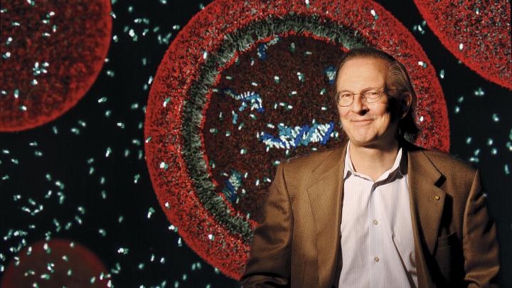 Jack Szostak, professor of chemistry and chemical biology and professor of genetics. Behind him is an illustration of a protocell, a vesicle containing fragments of RNA. 